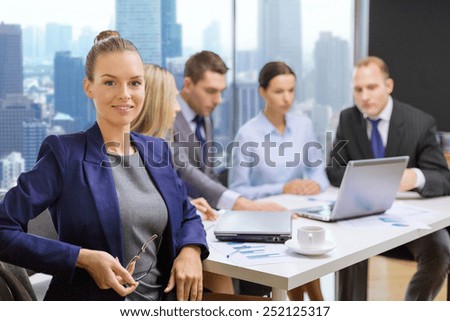 business, teamwork, technology and people concept - smiling businesswoman over team with laptop computer sitting in office