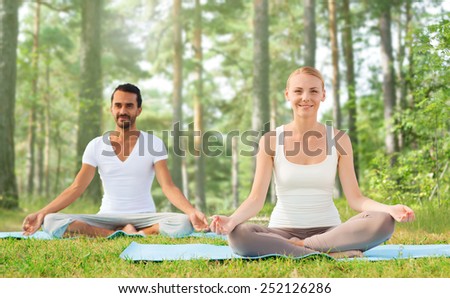 sport, fitness, yoga and people concept - smiling couple meditating and sitting on mats over green woods background