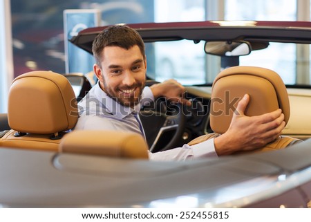 auto business, car sale, consumerism and people concept - happy man sitting in car at auto show or salon