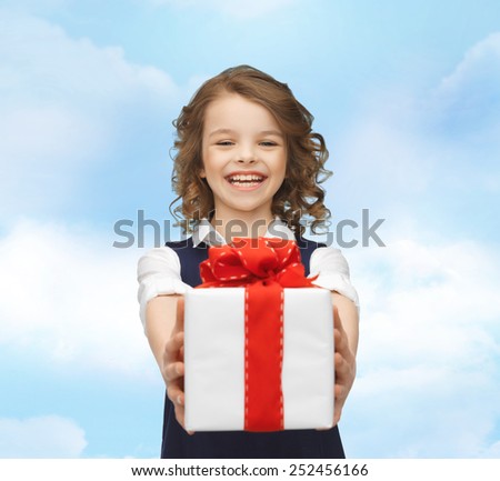 people, childhood, summer and holidays concept - happy smiling girl with gift box over blue sky background
