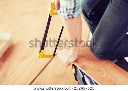 repair, building and home concept - close up of male hands cutting parquet floor board with saw