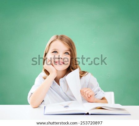 education, people, children and school concept - little student girl sitting at table with book over green chalk board background