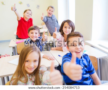 education, elementary school, learning, gesture and people concept - group of school kids sitting in classroom and showing thumbs up
