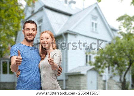 love, people, real estate, home and family concept - smiling couple hugging and showing thumbs up over house background