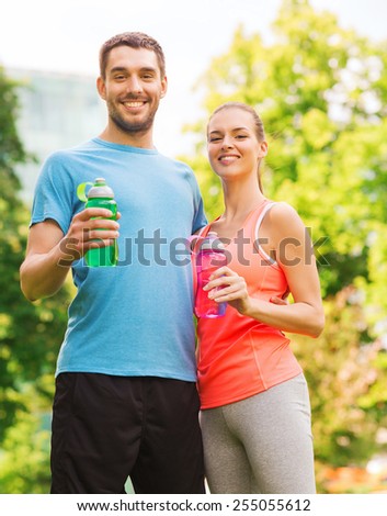 fitness, sport, friendship and lifestyle concept - smiling couple with bottles of water outdoors