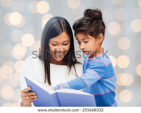family, children, education, school and happy people concept - happy mother and daughter reading book over holidays lights background