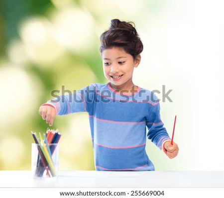 children, creativity and happy people concept - happy little girl drawing with coloring pencils over green background