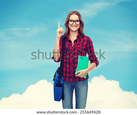 education and people concept - smiling female student in eyeglasses with bag and notebooks showing finger up over blue sky background