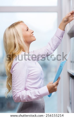 education, business, gesture, success and people concept - smiling businesswoman taking files from shelf in office