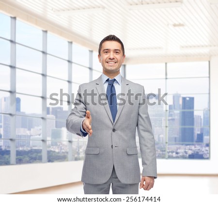 business people, gesture, partnership, real estate and greeting concept - happy smiling businessman in suit shaking hand over city office window background