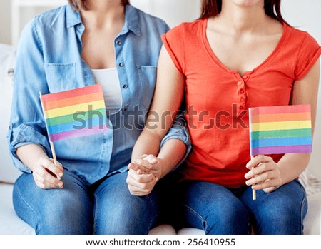 people, homosexuality, same-sex, gay pride and love concept - close up of happy lesbian couple holding rainbow flags at home