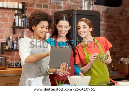 cooking class, friendship, food, technology and people concept - happy women with tablet pc computer in kitchen