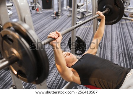 sport, bodybuilding, lifestyle and people concept - young man with barbell flexing muscles and making bench press in gym