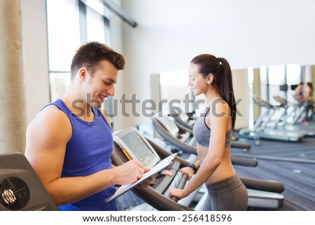 sport, fitness, lifestyle, technology and people concept - happy woman and trainer with clipboard working out on treadmill in gym