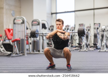 sport, bodybuilding, lifestyle and people concept - young man with barbell doing squats in gym