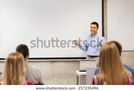 education, high school, technology and people concept - smiling teacher standing with remote control, laptop computer in front of white board and students in classroom