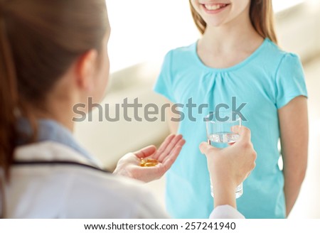 health care, people, children and medicine concept - close up of doctor giving capsules of cod-liver oil to happy girl at hospital