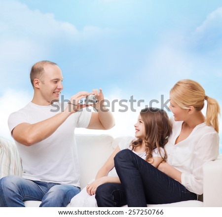 family, technology and people - smiling mother, father and little girl with camera over blue sky background