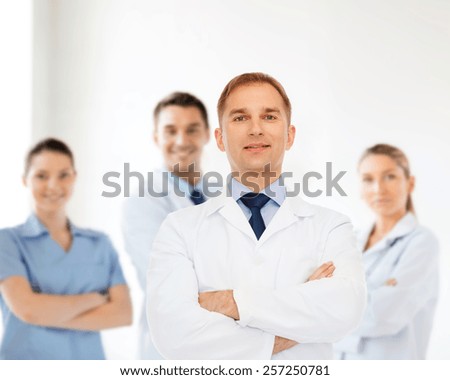 healthcare, profession, teamwork and medicine concept - smiling male doctor in white coat over group of medics
