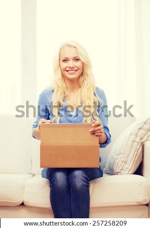 transportation, post and people concept - smiling young woman opening cardboard box at home