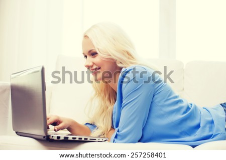 home, technology and internet concept - smiling woman lying on the couch with laptop computer at home