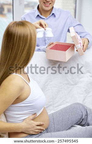 pregnancy, family, people and expectation concept - close up of happy pregnant woman showing babys bootees to man or husband at home