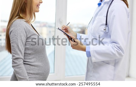pregnancy, healthcare, people and medicine concept - close up of happy pregnant woman and doctor with clipboard at medical appointment in hospital