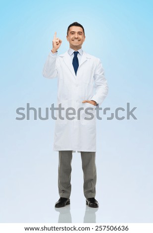 healthcare, profession, people and medicine concept - smiling male doctor in white coat pointing finger up over blue background