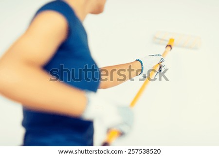 interior design and home renovation concept - woman with roller and paint colouring the wall