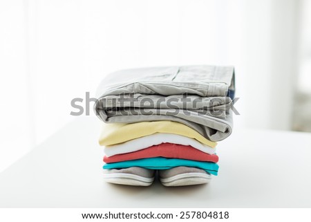 clothes, personal staff and objects concept - close up of folded shirts, pants and shoes on table at home