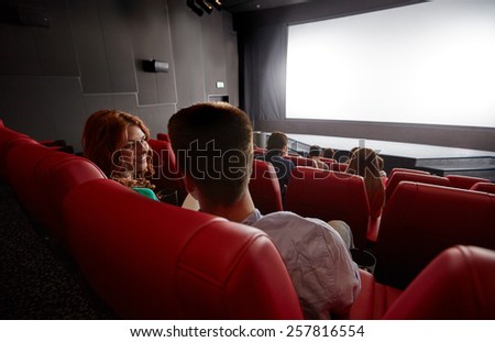 cinema, entertainment, communication and people concept - happy couple of friends watching movie and talking in theater from back