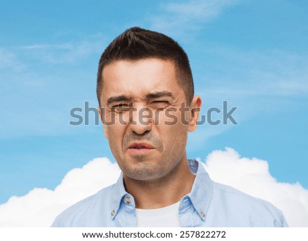 emotions, facial expression and people concept - man wrying of unpleasant smell over blue sky and cloud background