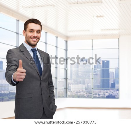 business, people and office concept - happy young businessman showing thumbs up over office room or new apartment background