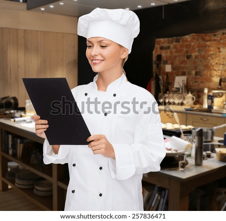 cooking, bakery, people, advertisement and food concept - smiling female chef cook or baker with blank black menu paper over restaurant kitchen background
