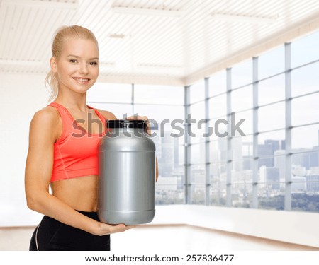 sport, fitness, food additive and people concept - smiling young woman holding protein jar over gym or home background