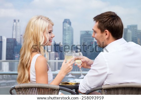 summer holidays, people, honeymoon, vacation and dating concept - couple drinking wine in cafe over city background