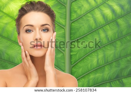 beauty, people and health concept - beautiful young woman touching her face over green palm leaf background