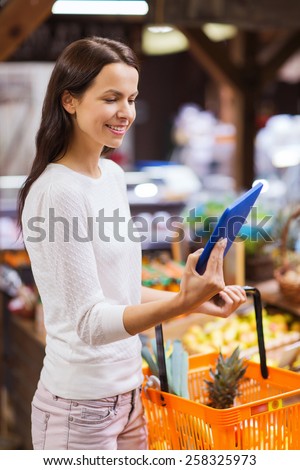 sale, shopping, consumerism and people concept - happy young woman with food basket and tablet pc computer in market