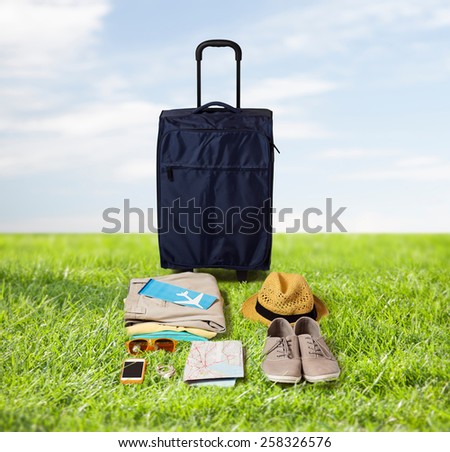 summer vacation, tourism and objects concept - travel bag, map, air ticket and clothes with personal stuff over blue sky and grass background