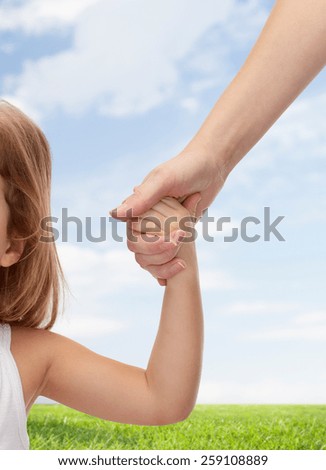 people, charity, family and adoption concept - close up of woman and little girl holding hands over blue sky and grass background
