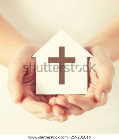religion, christianity and charity concept - female hands holding paper house with christian cross symbol