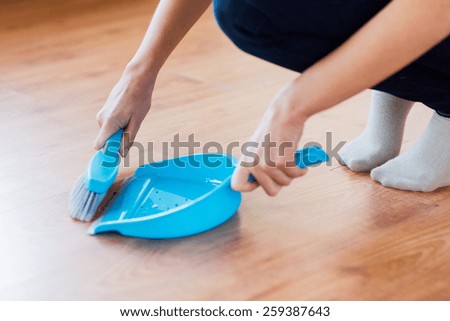 people, housework, cleaning and housekeeping concept - close up of woman with brush and dustpan sweeping floor at home