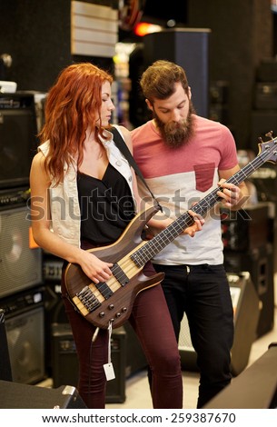 music, sale, people, musical instruments and entertainment concept - happy couple of musicians with bass guitar at music store