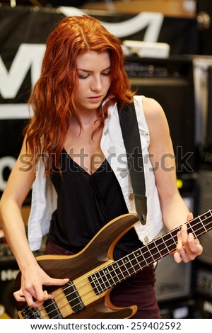 music, sale, people, musical instruments and entertainment concept - female musician or customer playing bass guitar at music store