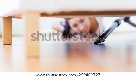 people, housework and housekeeping concept - close up of happy woman with vacuum cleaner cleaning floor under couch at home