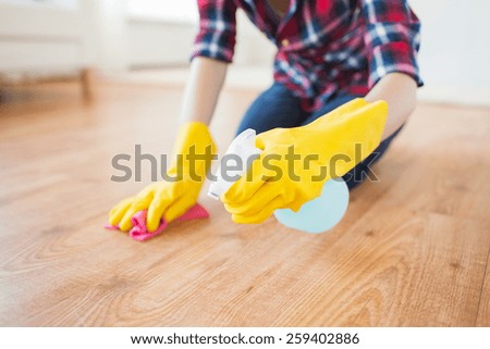 people, housework and housekeeping concept - close up of woman in rubber glover with cloth and detergent spray cleaning floor at home