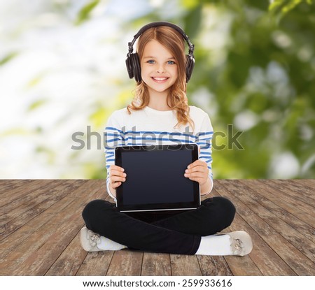 music, technology, people and childhood concept - happy girl with headphones showing tablet pc computer blank screen over greed background