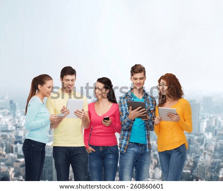 friendship, technology and people concept - group of smiling teenagers with smartphones and tablet pc computers over city background