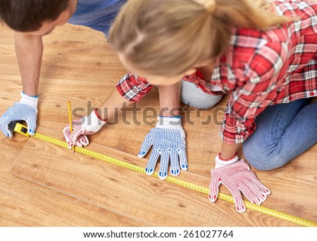 repair, building, flooring and people concept - happy couple with ruler measuring parquet board at home