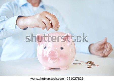 savings, oldness, business, people and banking concept - close up of senior man hands putting coins into piggy bank